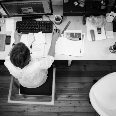 Black and white image of an employee working at a desk with papers and computer.